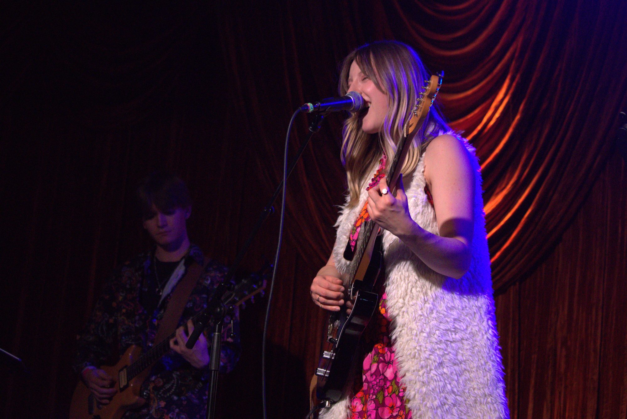 Piper Madison singing on stage in front of a red velvet curtain